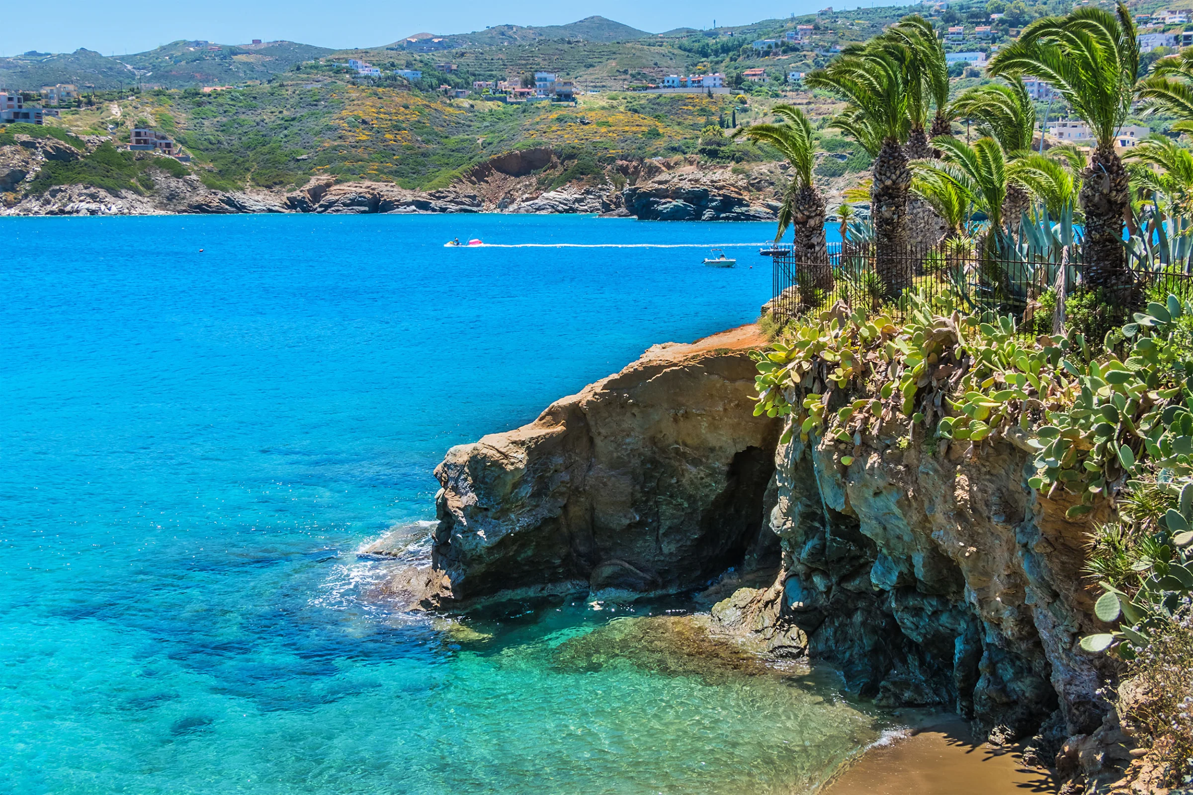 Wide aerial or elevated view of Agia Pelagia Beach and the sheltered bay, showing the bay curve, clear water, and the villag