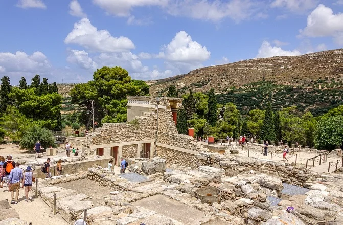 Visitors walking the open, unshaded paths of the Knossos site in strong midday light.