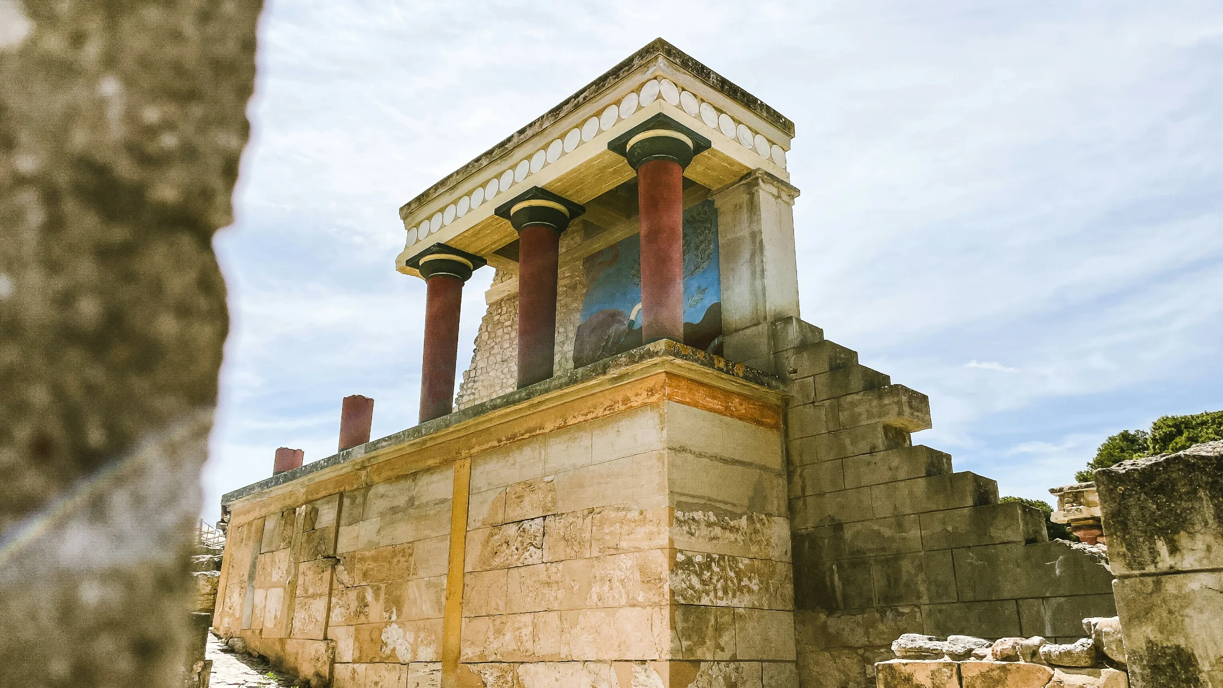 Visitors walking the path through Knossos Palace with the reconstructed throne room walls and Minoan frescoes visible in the